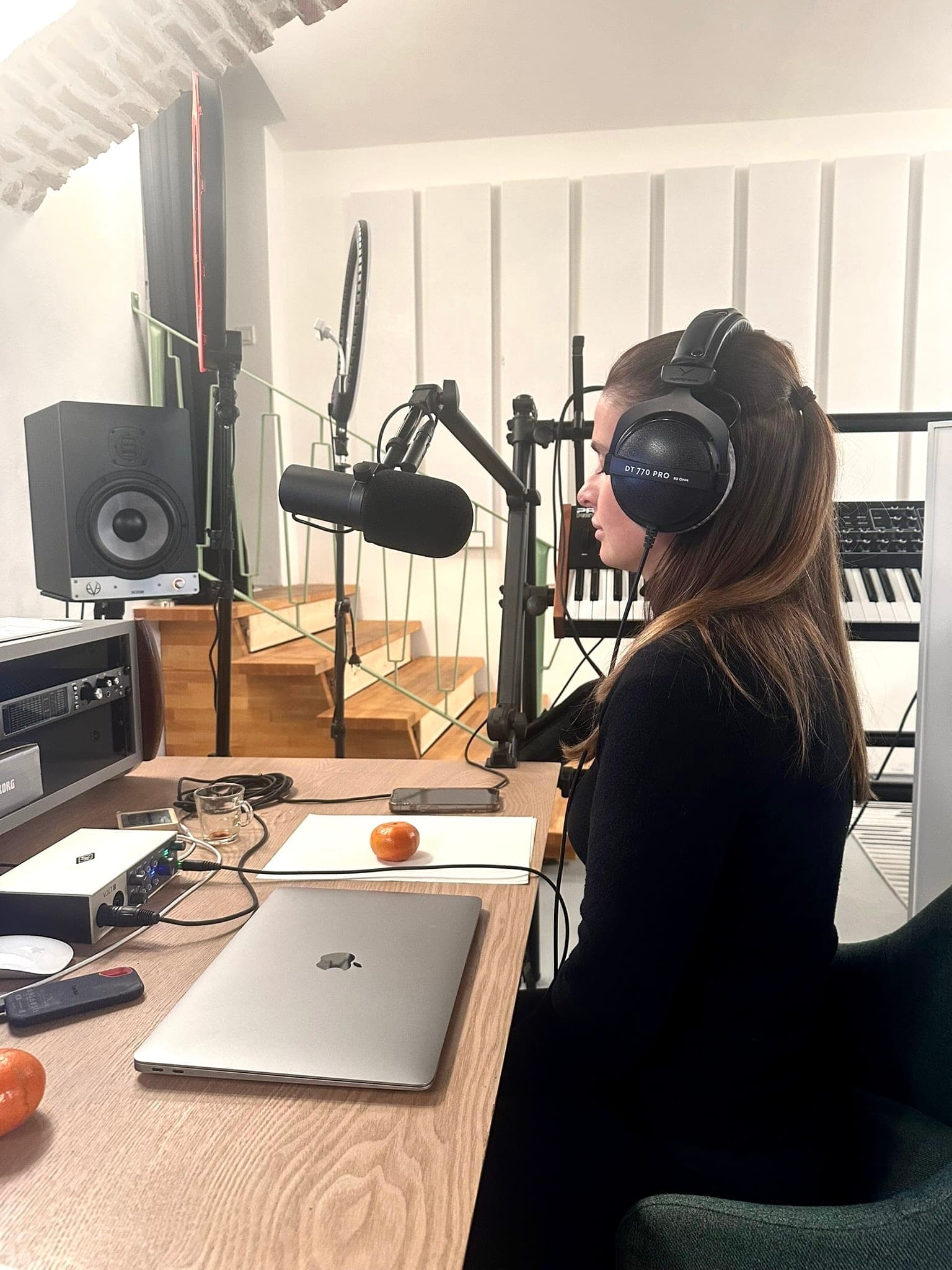 At the mixing desk with headphones, laptop and microphone in front.