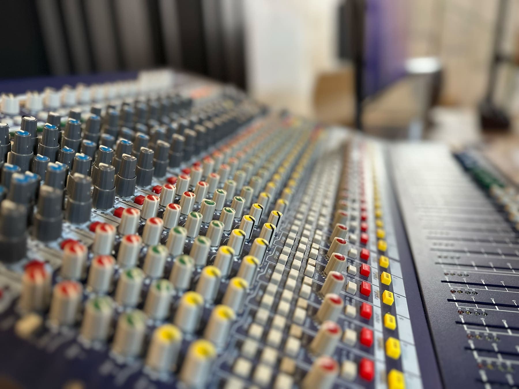 Close-up of the mixing desk with rows of colourful knobs and faders.