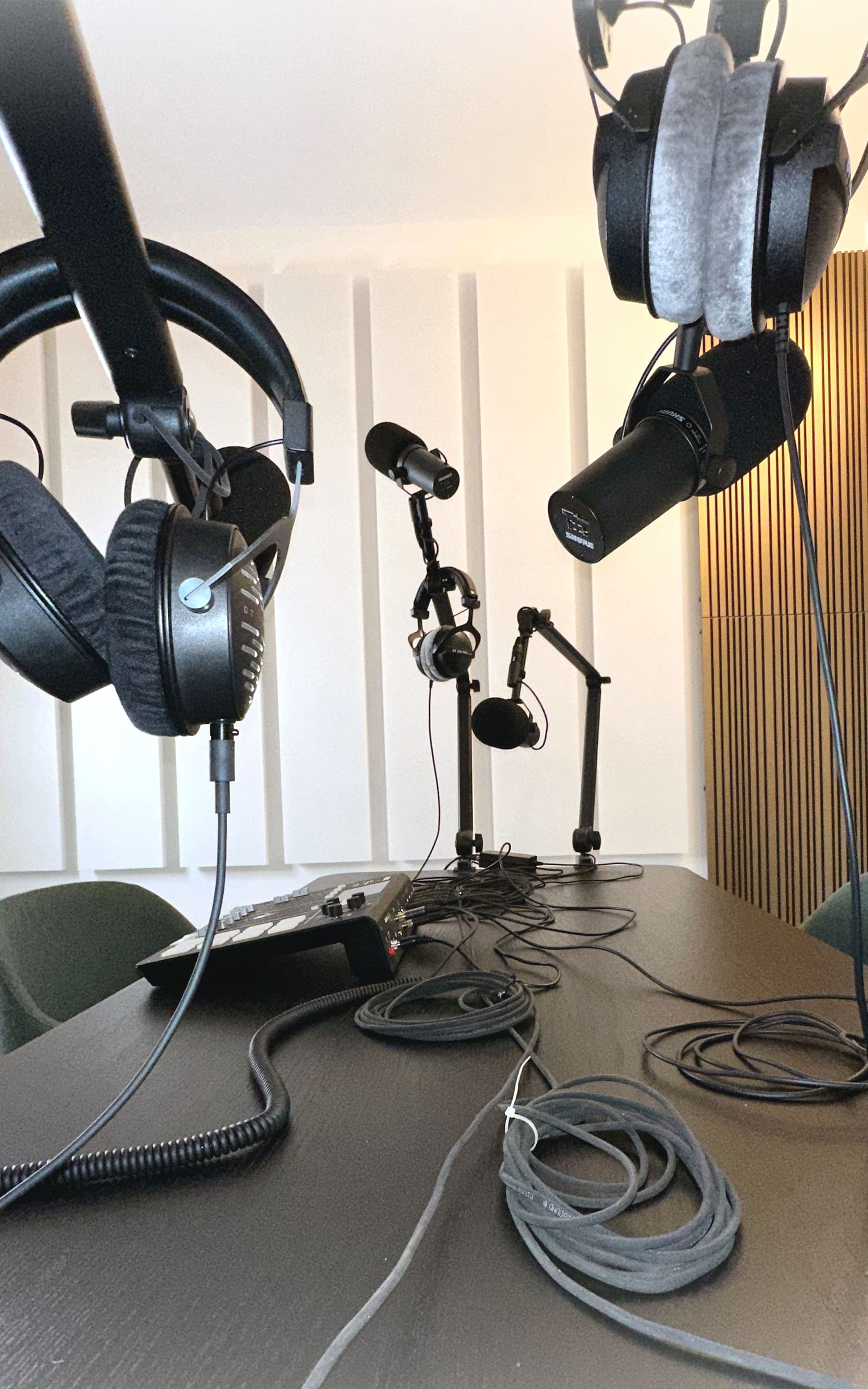 Two pairs of headphones hang above the podcast table, with microphones and coiled cables behind them.