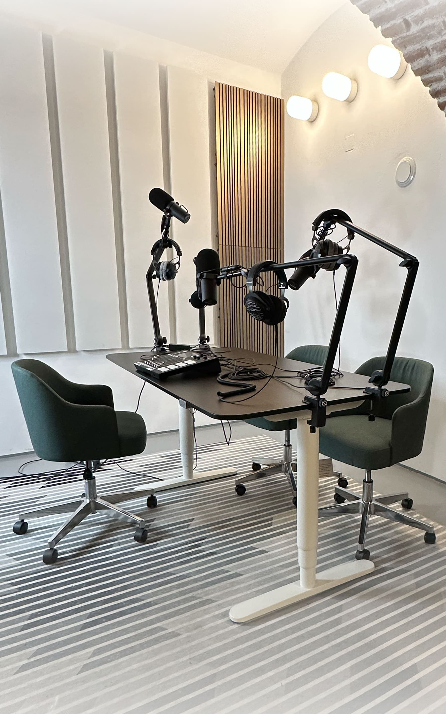 The podcast corner: a black table with three microphones on arms, headphones and a recorder, surrounded by three green armchairs.