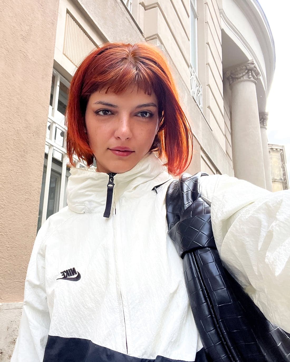 Wered Fuchs with red hair and a white jacket in front of a pale building wall.